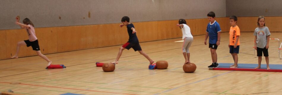 Kinder balancieren auf Gymnastikgeräten in einer Turnhalle.