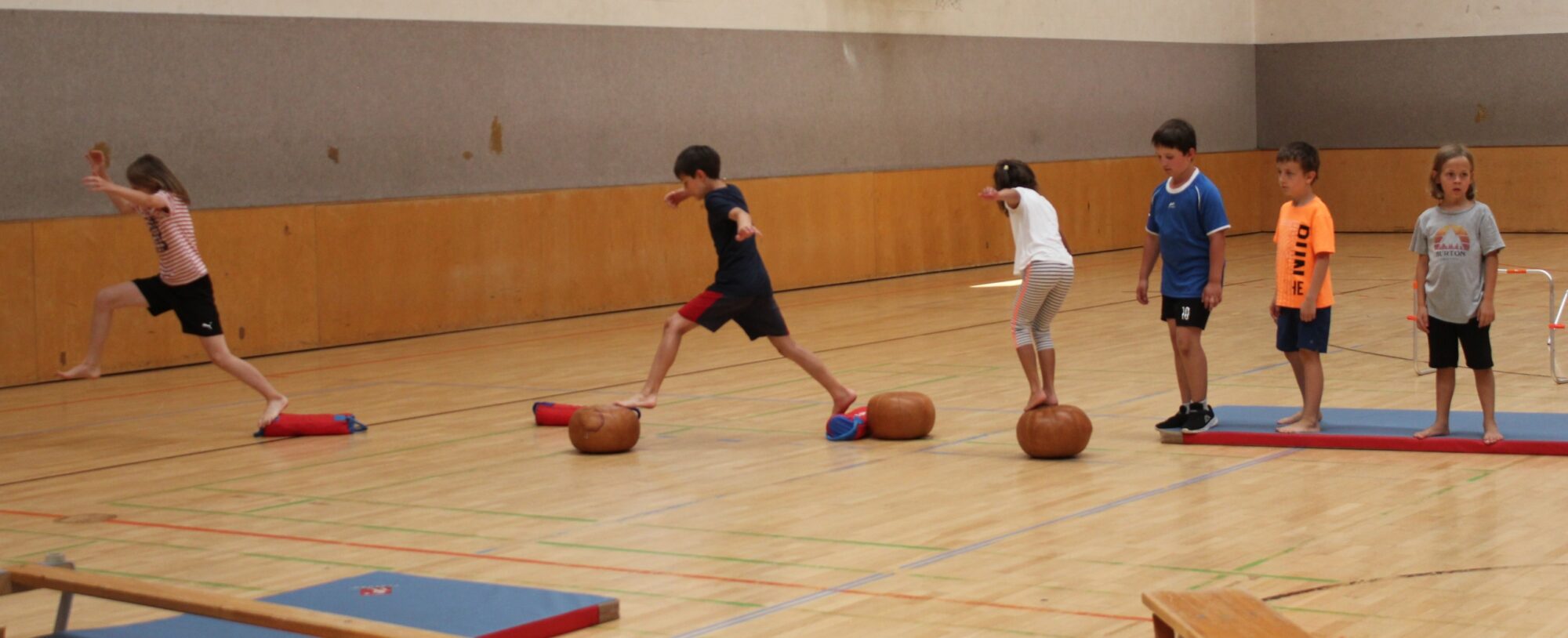 Kinder balancieren auf Gymnastikgeräten in einer Turnhalle.