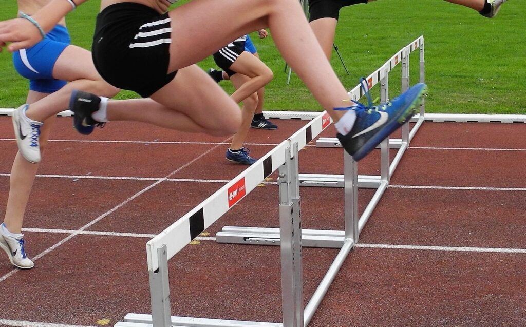 Mehrere junge Athletinnen springen gleichzeitig über Hürden auf einer roten Tartanbahn bei einem Leichtathletikwettkampf.