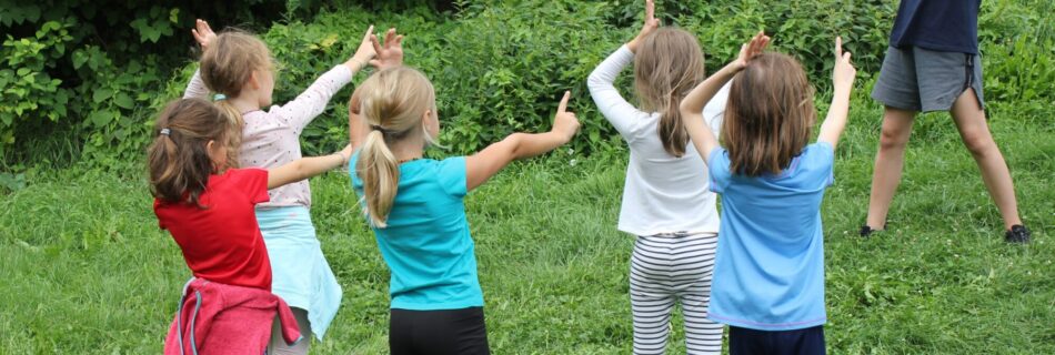 Eine Gruppe von Kindern macht Bewegungsübungen im Freien unter Anleitung eines Erwachsenen.