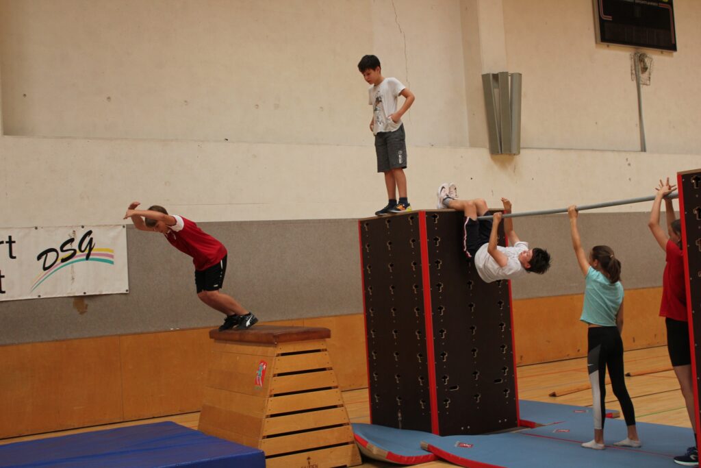 Kinder bewältigen eine Hindernisstrecke in einer Turnhalle mit Sprüngen und Kletterelementen.