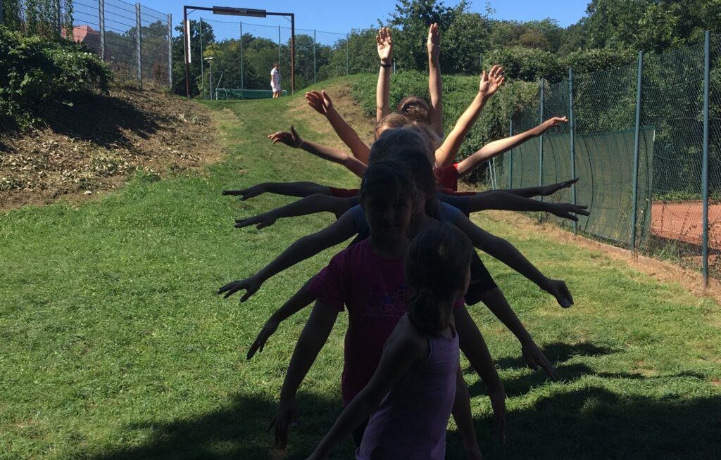 Mehrere Kinder stehen in einer Linie hintereinander, sodass ihre ausgestreckten Arme wie ein Fächer wirken.